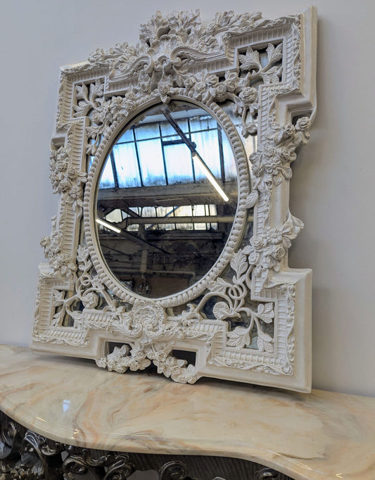 Decorative white mirror with intricate carvings on a marble surface.